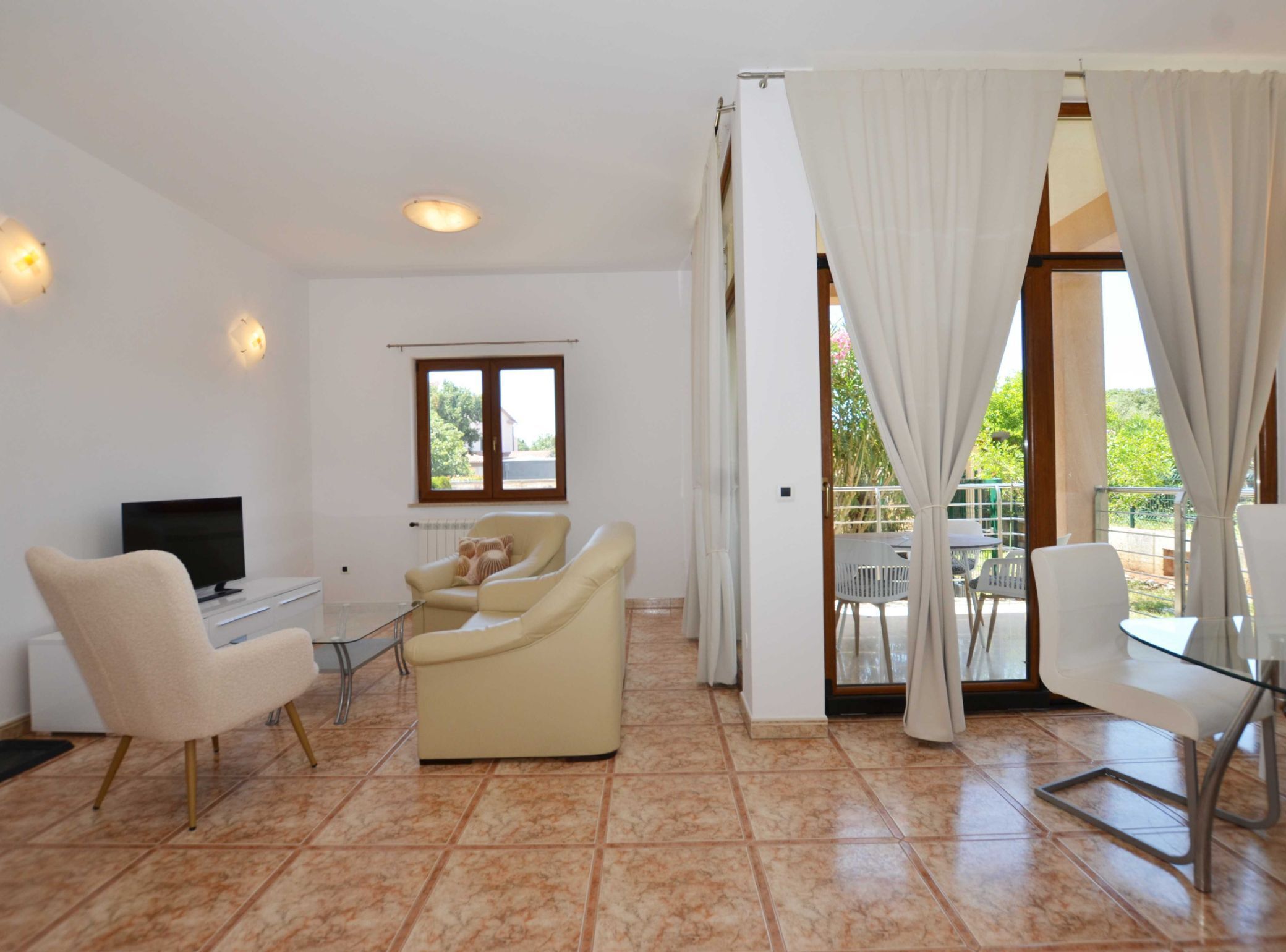A modern living room with a TV, two sofas, a glass table, and a balcony with outdoor seating.