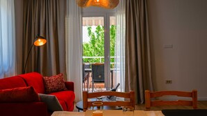 A room with a red sofa, a dining table with a glass of orange juice, a wicker pendant light, and a view of greenery through a sliding door. - Modern and Stylish Rovinj Apartments With Terrace (Rovinj)