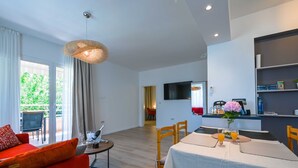 A modern living room with a sofa, a dining table set for two, and a kitchen area with a TV and a fruit display. - Modern and Stylish Rovinj Apartments With Terrace (Rovinj)
