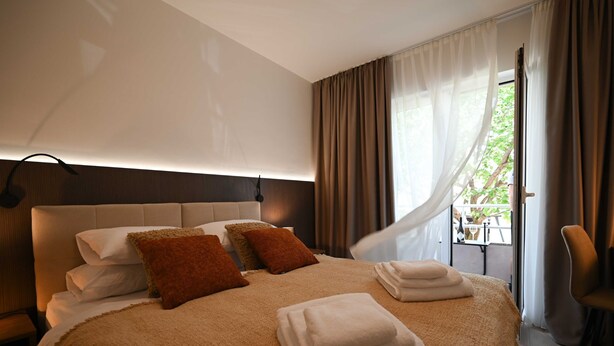 A modern hotel room with a large bed, a headboard, a bedside table, a chair, and a window with curtains. - Modern and Stylish Rovinj Apartments With Terrace (Rovinj)