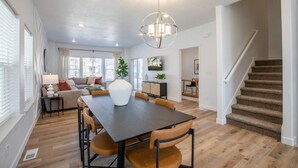 Een ruime woonkamer met een donkere houten eettafel, zachte zitplaatsen en een moderne kroonluchter.