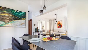 A dining area with a grey table, black chairs, and a fruit platter. There is a painting on the wall and a sofa in the background.