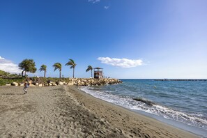 A beach with a lifeguard tower, palm trees, and a rocky breakwater. - Agios Tychon Luxury Villa With Private Pool (Limassol)