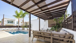 A covered outdoor area with a pool, a sofa, and potted plants.
