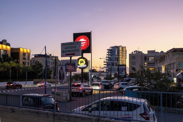 A busy urban street at dusk with multiple cars and a pharmacy sign. - Agios Tychon Luxury Villa With Private Pool (Limassol)