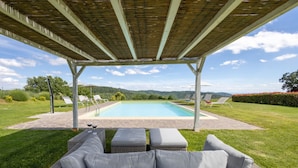 Uma área externa coberta com piscina, espreguiçadeiras e um sofá de vime.