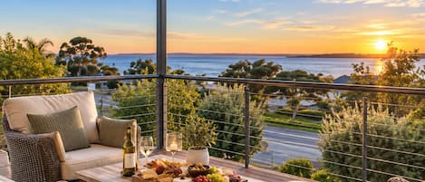 A balcony with wicker furniture, a table with a wine bottle, and a sunset view.