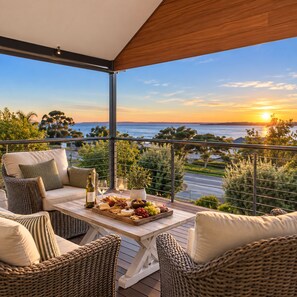 A balcony with wicker furniture, a table with a wine bottle, and a sunset view.
