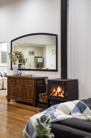 A modern living room with a wooden cabinet, a large mirror, and a black wood-burning stove. - Waterfront Retreat | Estuary Views & Balcony (Dawesville)