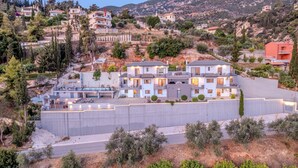 A hillside residential area with modern houses, a large white building with multiple balconies, and a prominent concrete retaining wall.