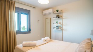 A hotel room with a bed, a window with curtains, a wall-mounted air conditioner, and a shelf with decorative items.