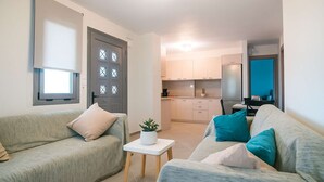 A modern living room with a sofa, a small table with a plant, and a kitchen in the background.