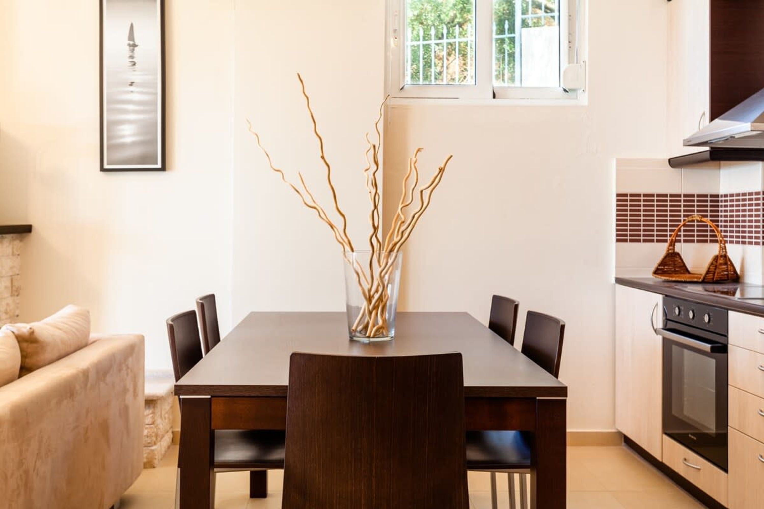 A dining area with a dark wooden table, six chairs, and a vase with branches.