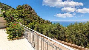 Un balcon offrant une vue sur un paysage côtier, comprenant une colline et la mer.