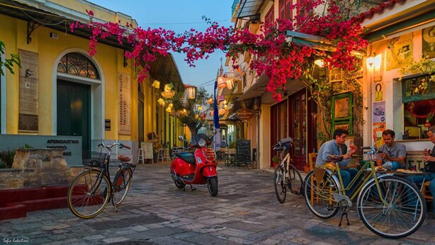 A narrow street with buildings on either side, a red scooter parked in the middle, and people sitting at outdoor tables. - Uncover Kalamata s Hidden Gem - Cosy City Nest (Kalamata)