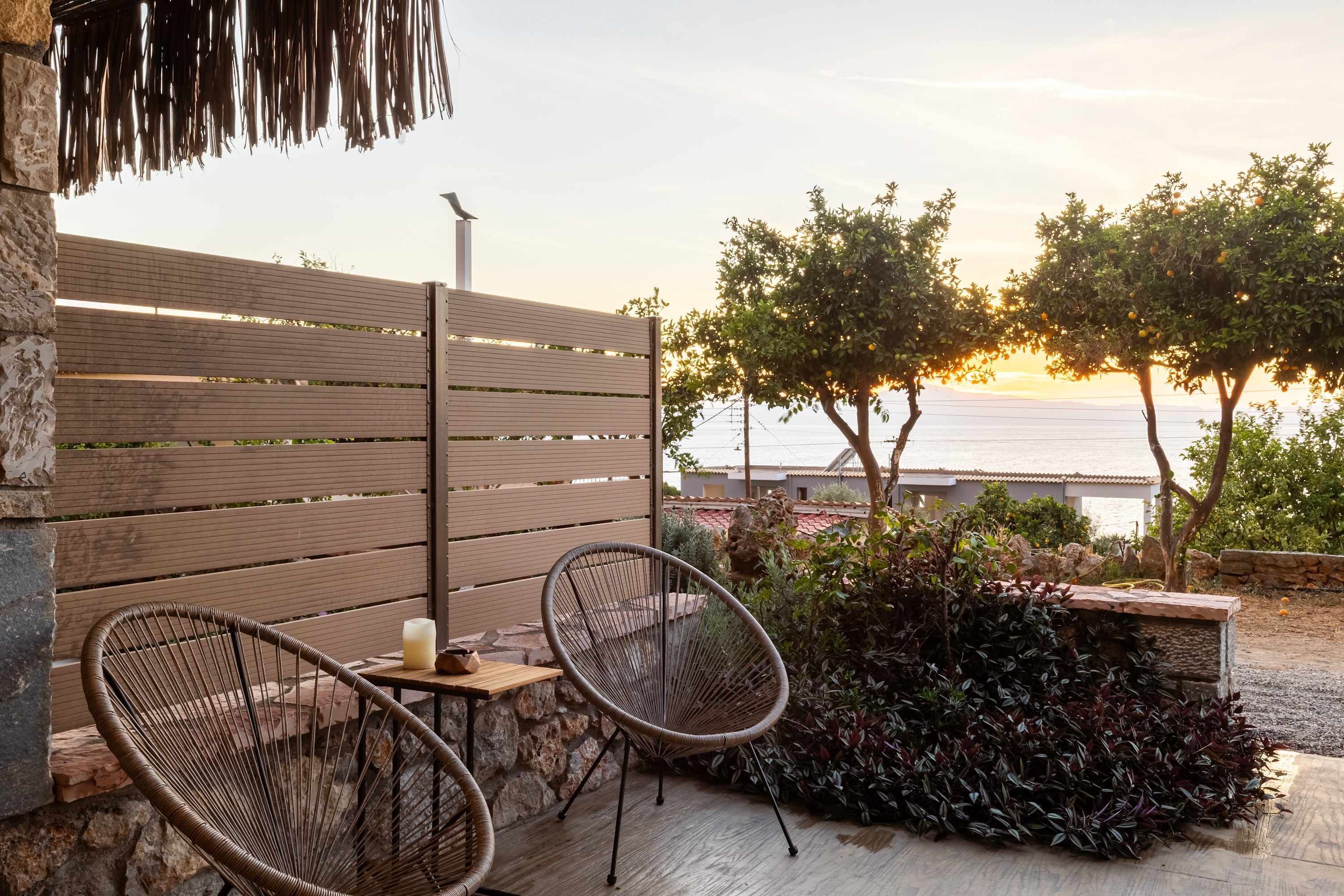 Une terrasse avec deux fauteuils en osier, une petite table avec une bougie et une vue sur la mer au coucher du soleil.
