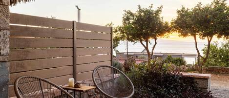 Une terrasse avec deux fauteuils en osier, une petite table avec une bougie et une vue sur la mer au coucher du soleil.