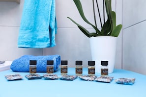 Casa de banho com toalha azul, uma planta em vaso e várias embalagens de essência de tratamento facial.