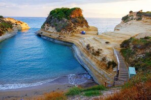 Paisagem costeira com um canal estreito, uma escadaria de madeira e uma pequena construção em um penhasco.