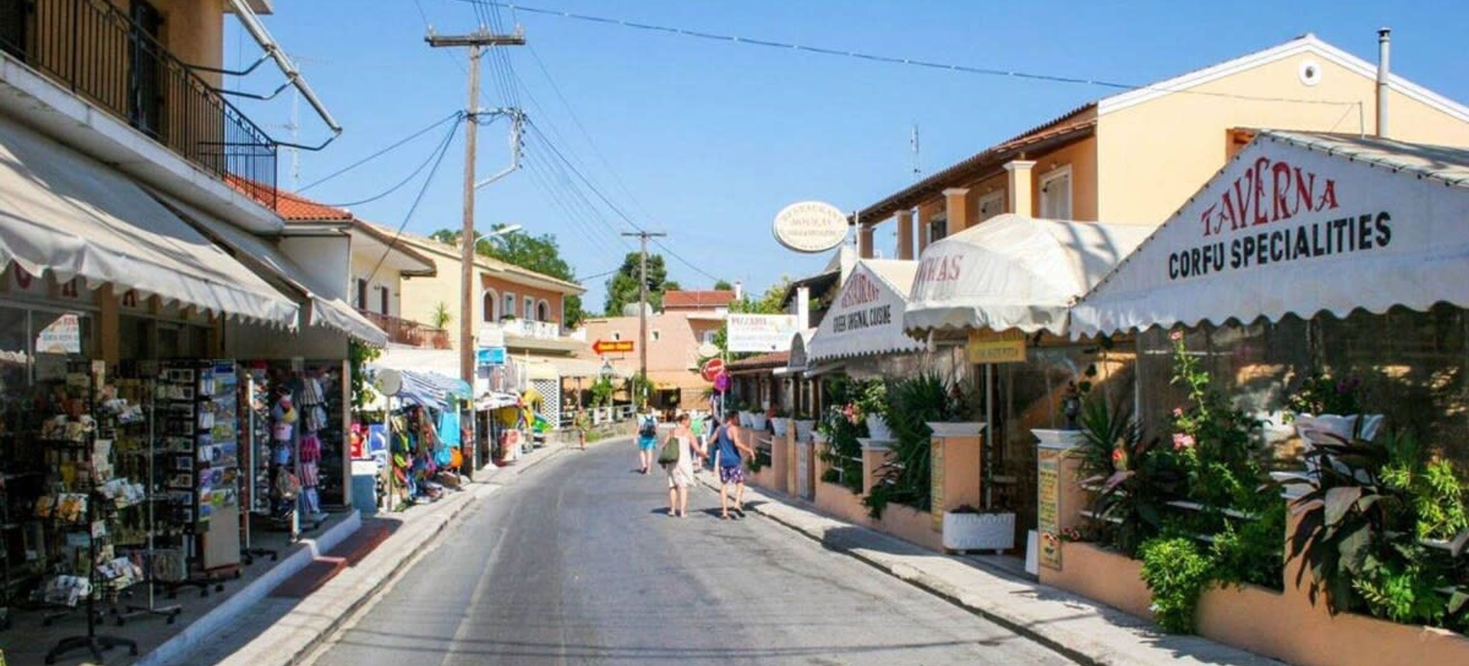 Een straat met winkels en een restaurant genaamd 'Taverna Corfu Specialities'.