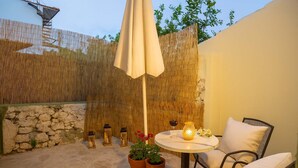 Un espace patio comprenant une table ronde, deux chaises, un parasol blanc, des plantes en pot et des lanternes décoratives.