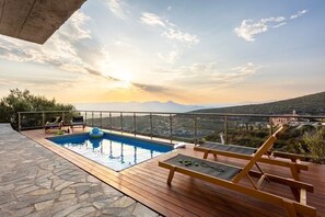 Una piscina en la azotea con terraza de madera y sillones de descanso, con vistas a un paisaje montañoso.