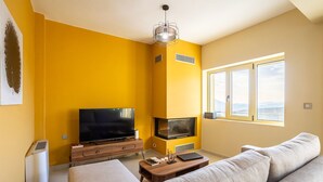 A living room with a yellow wall, a flat-screen TV, a fireplace, a sofa, and a window with a view. - Martinia Pool Escape - Tragos Panoramic Views (Kalamata)