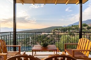 Een balkon met houten stoelen en een tafel, met uitzicht op een bergachtig landschap.
