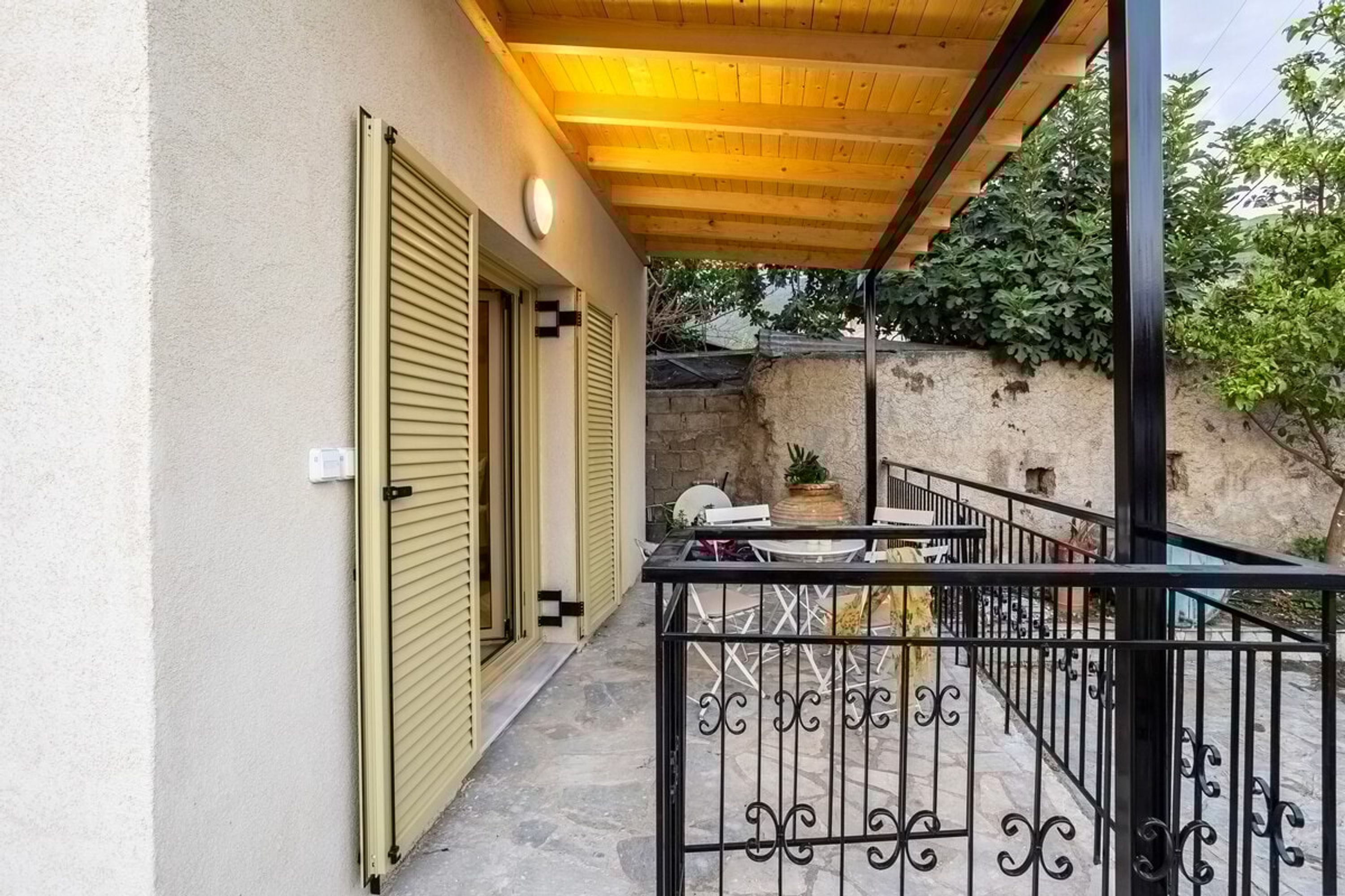 A covered outdoor area with a wooden ceiling, a metal railing, and a stone wall in the background.
