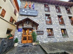 Un bâtiment en pierre avec une entrée en bois, des balcons ornés de jardinières et des drapeaux.