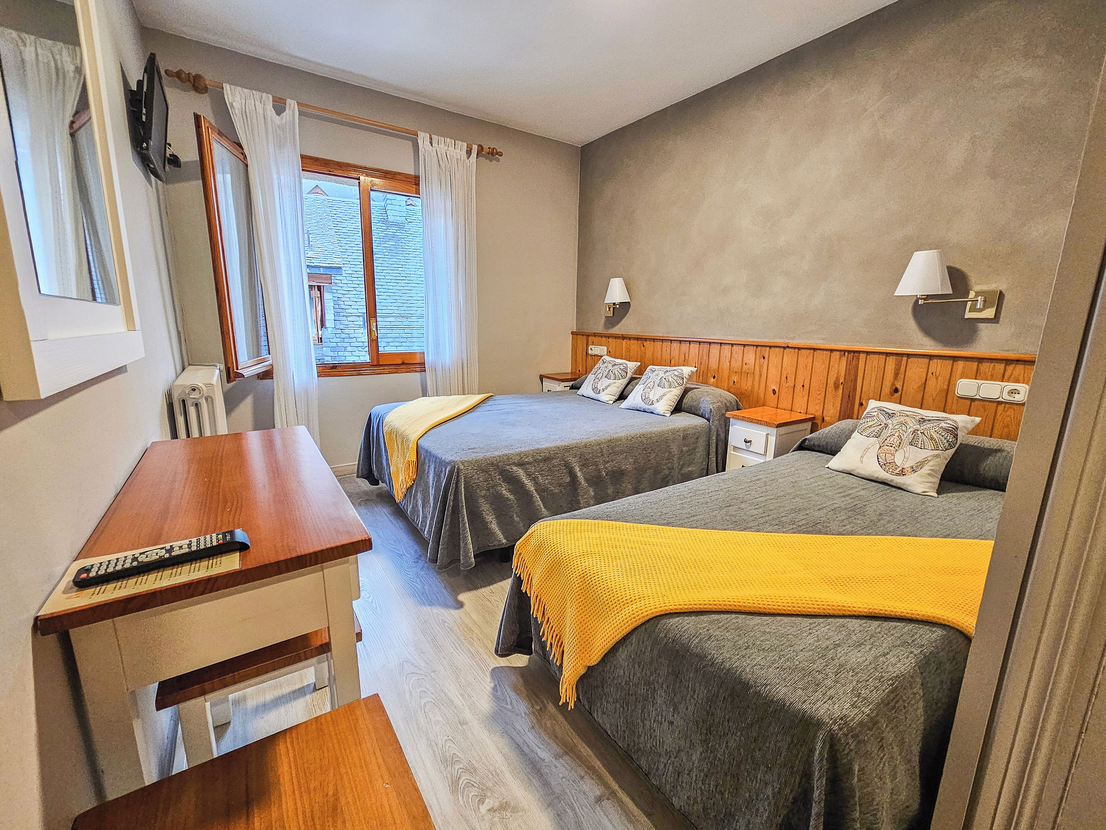 Een hotelkamer met twee bedden, een houten bureau, een televisie en een raam met gordijnen.