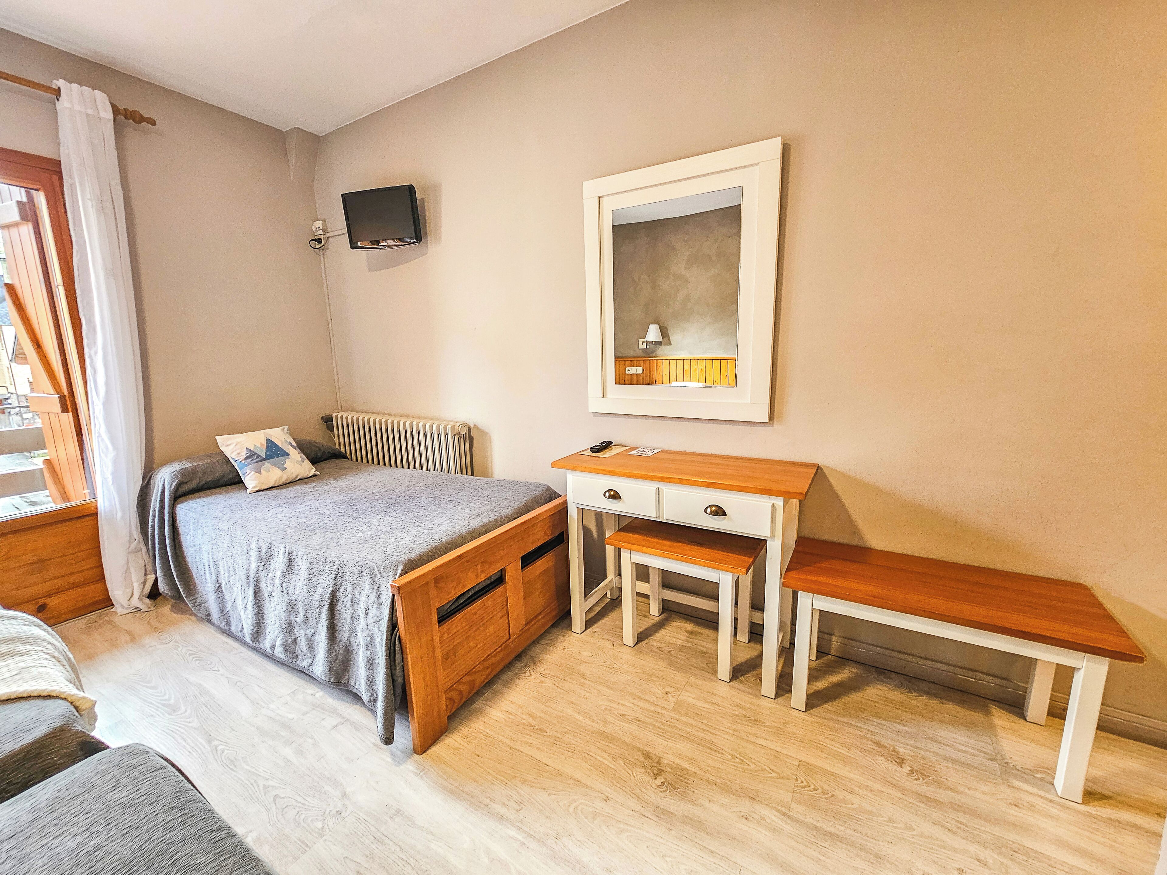 Un dormitorio con una cama, un escritorio, una silla, un televisor y una ventana con cortinas.