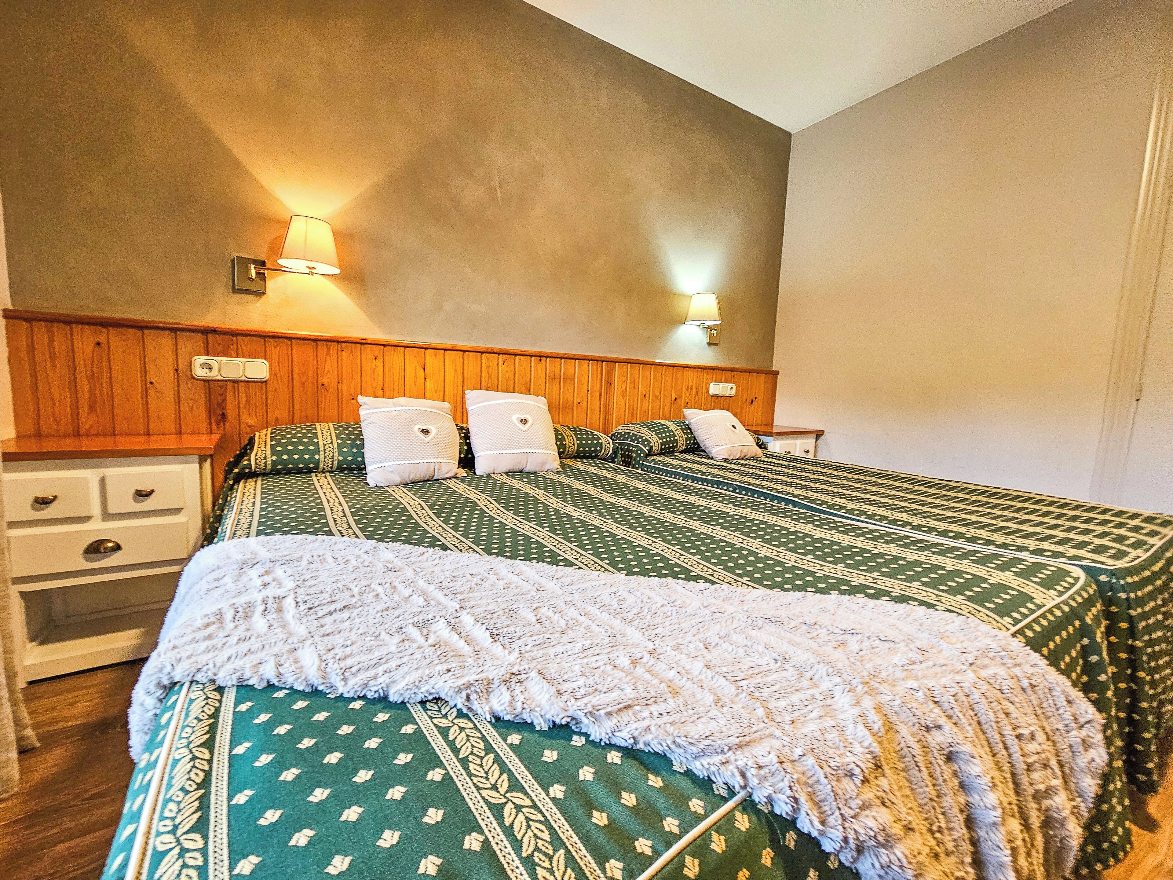 A bedroom with two beds, wooden headboard, bedside lamps, and a nightstand.