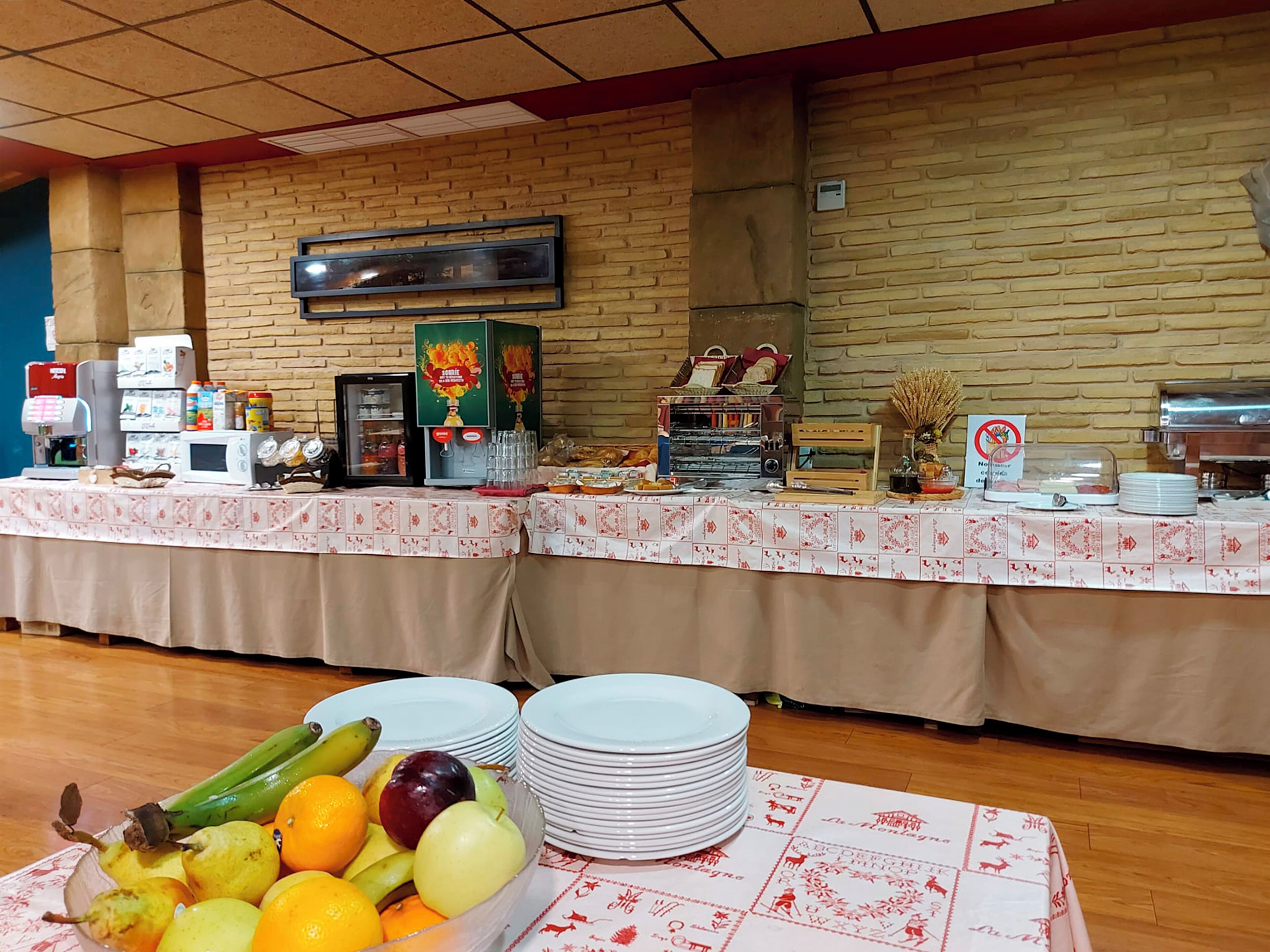 Een buffetopstelling met diverse gerechten en dranken, waaronder een schaal fruit, borden en een koffiehoek.