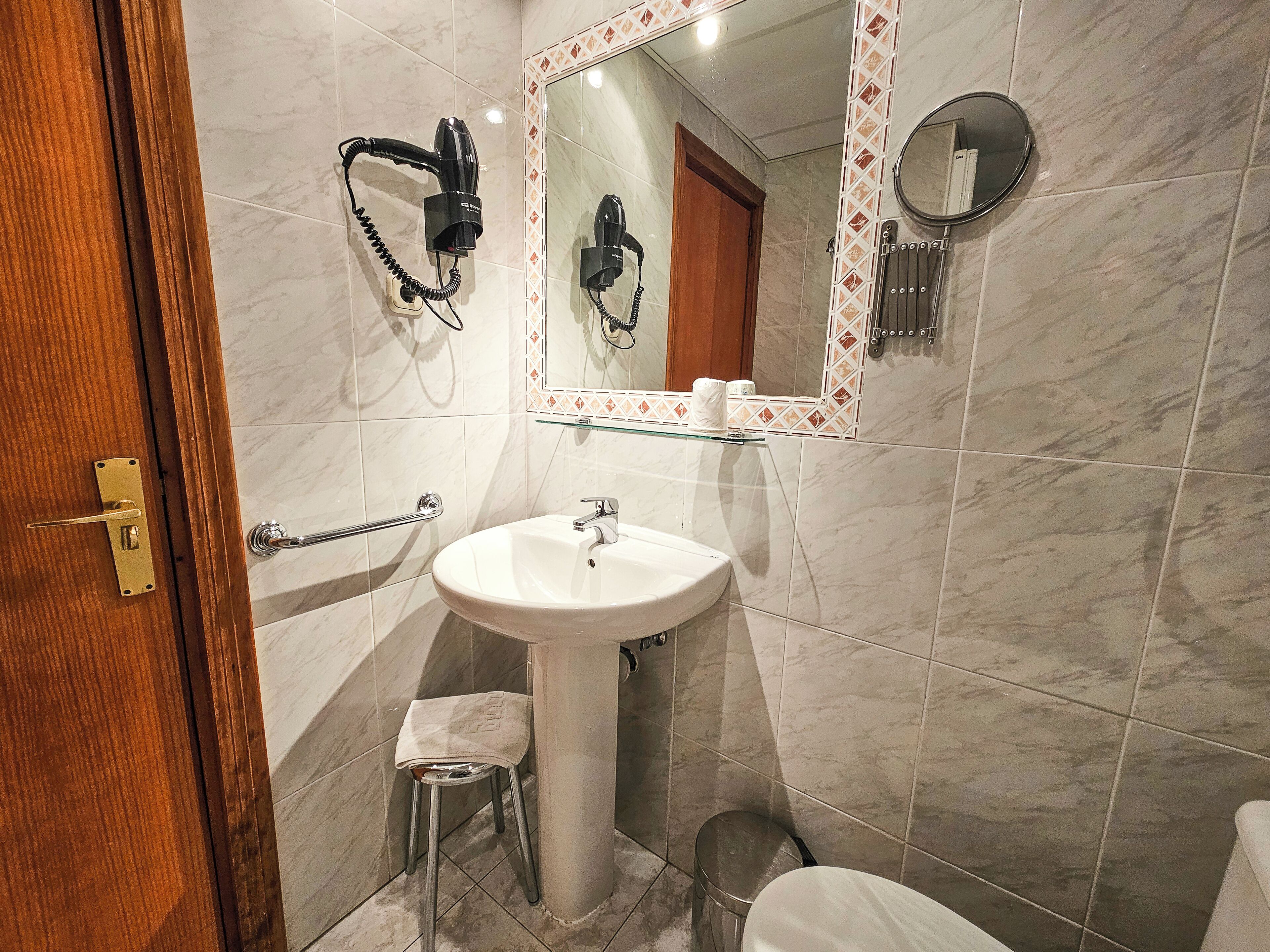 Een badkamer met een betegelde wand van marmer, een witte wastafel, een haardroger, een spiegel en een toilet.