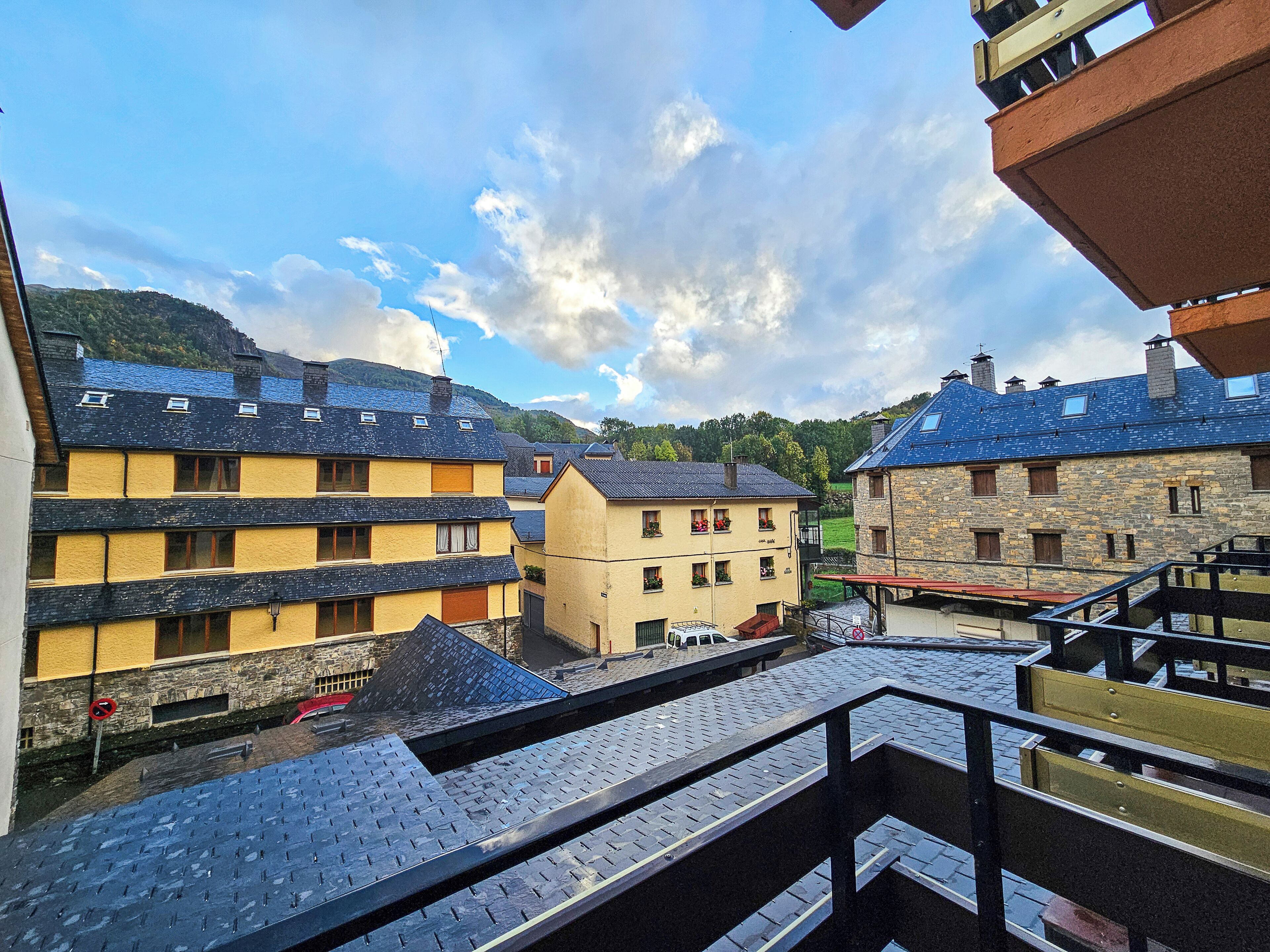 Blick auf eine Stadt mit Gebäuden mit Stein- und Holzfassaden, einem klaren Himmel und einer entfernten Bergkette.