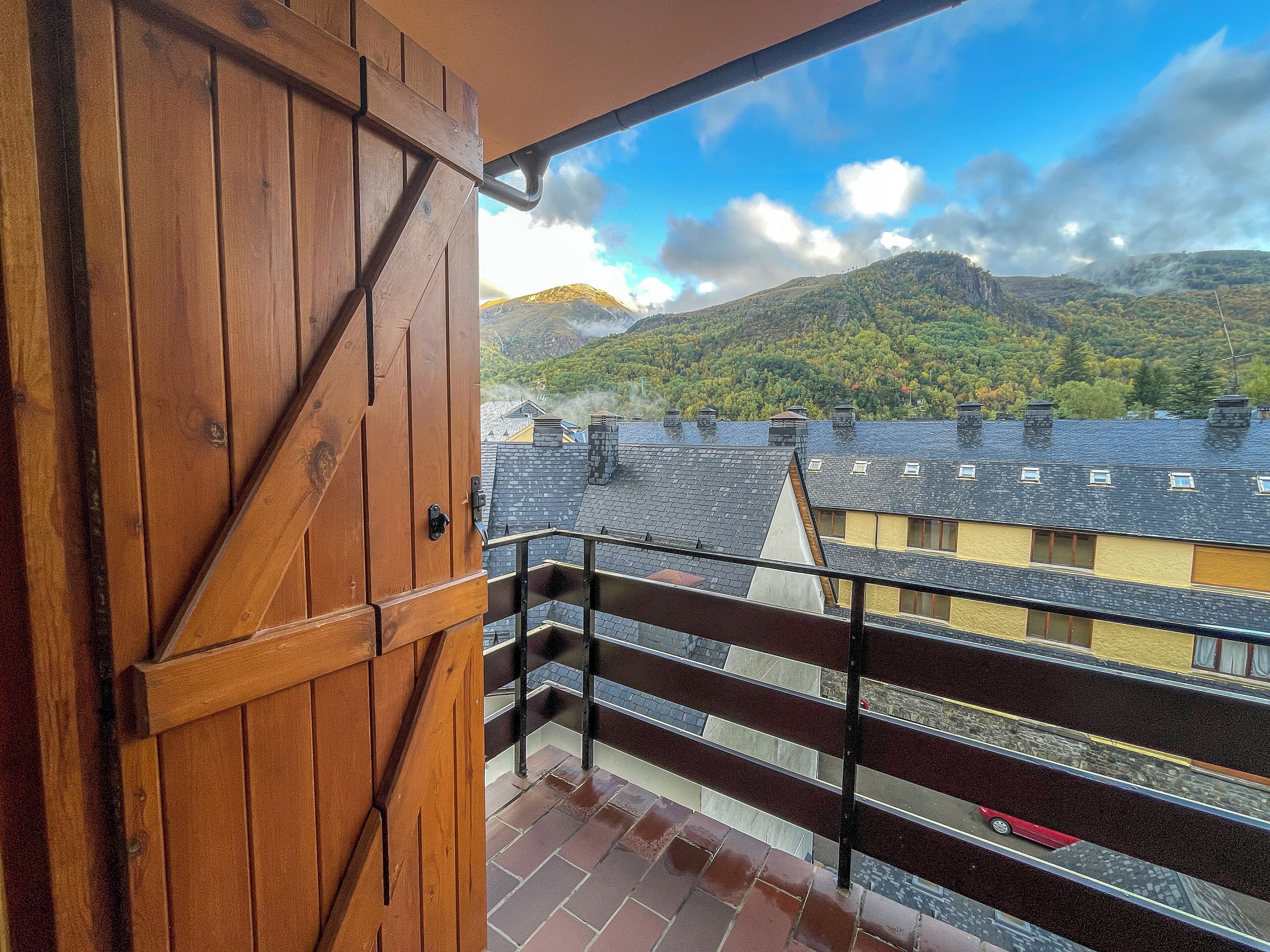A wooden door leading to a balcony with a view of a mountain and residential buildings.