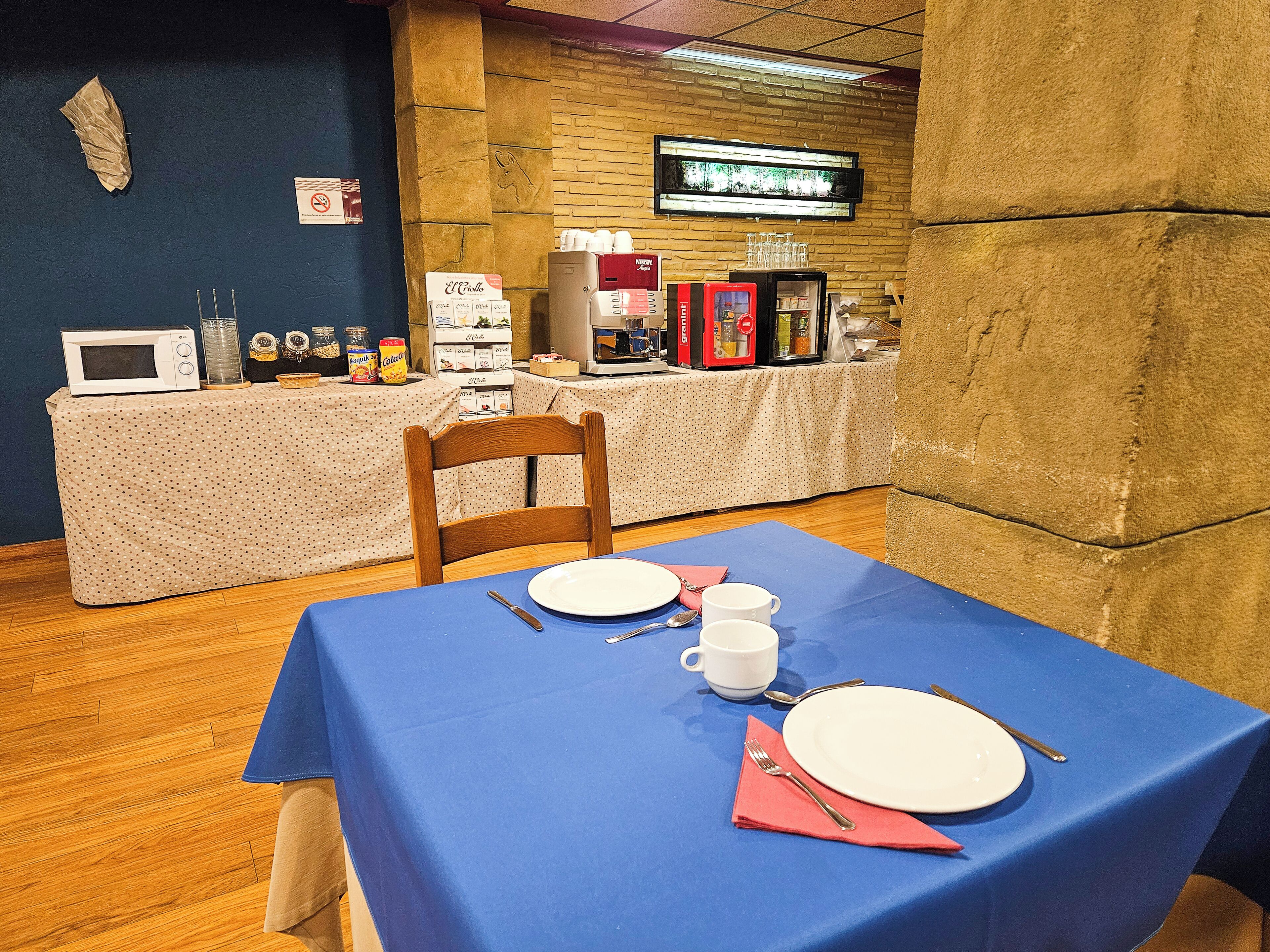 A dining area with a blue tablecloth, a wooden chair, and a microwave on a table.