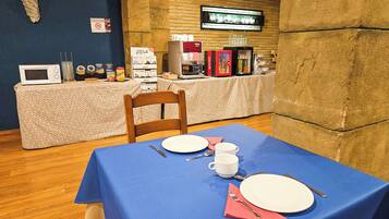 A dining area with a blue tablecloth, a wooden chair, and a microwave on a table.