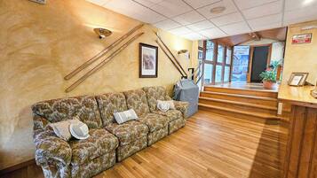 A reception area with a wooden reception desk, a floral-patterned sofa with cushions, a framed picture on the wall, and a staircase leading to an upper floor.