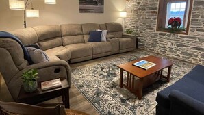 Un salón con sofá, sillón, mesa de centro y pared de piedra.
