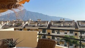 A balcony with wicker furniture, a round table, and a hanging light fixture. - 2-bed Sea View Apt, 10 Mins From Puerto Banus (Marbella)