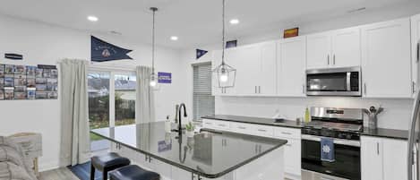 A modern kitchen with white cabinets, a large island with bar stools, stainless steel appliances, and a view of the outdoors.