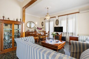 Un salon comprenant un canapé, une table basse en bois, une table à manger avec des chaises, un téléviseur et un meuble avec des portes en verre.