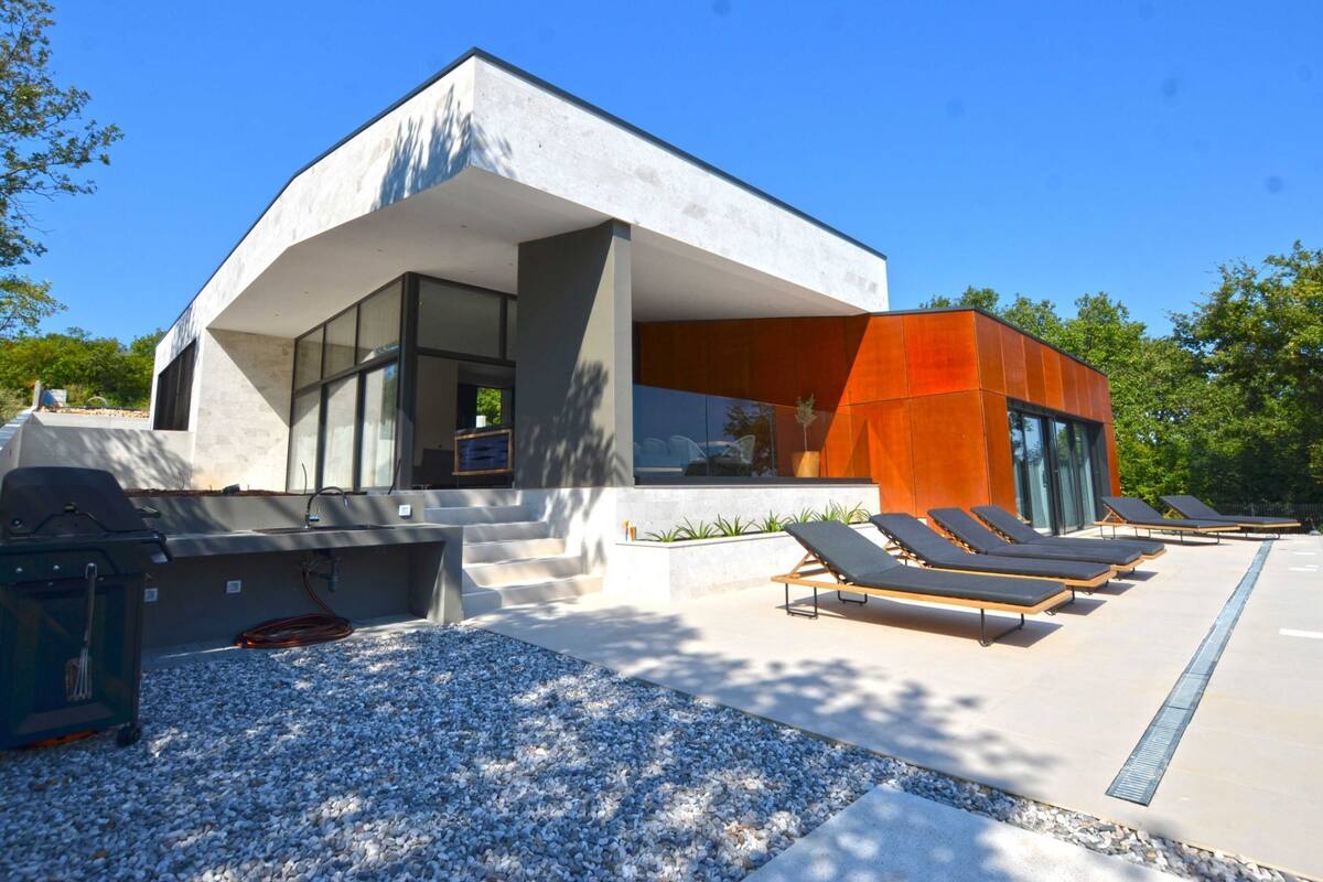A modern building with a large patio area featuring lounge chairs and a barbecue grill.