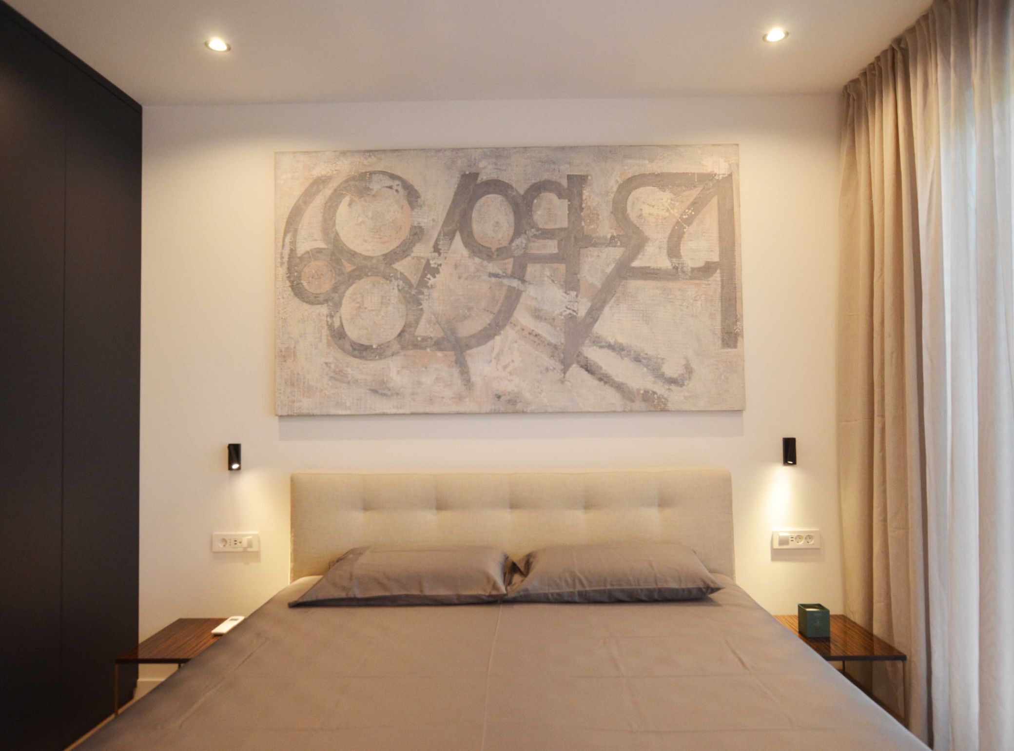 Une chambre à coucher moderne avec un grand lit, une tête de lit, deux tables de chevet et une œuvre d’art accrochée au mur.