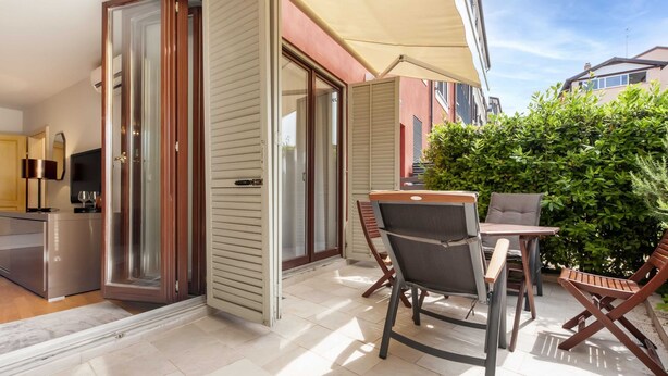 A modern outdoor patio area with a sliding glass door leading to a balcony, a small table with chairs, and a large umbrella providing shade. - Charming Bright Gem Rovinj Downtown (Rovinj)