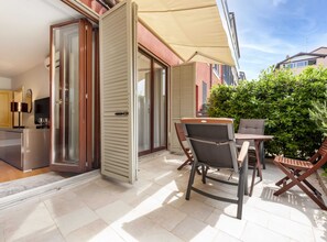 Een modern terras buiten, met een schuifpui naar een balkon, een kleine tafel met stoelen en een grote parasol voor de schaduw.