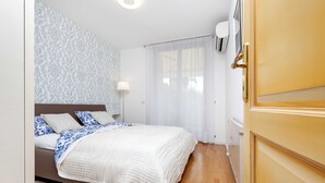 A bedroom with a bed, a bedside table, a lamp, a window with curtains, and a wall-mounted air conditioner. - Charming Bright Gem Rovinj Downtown (Rovinj)