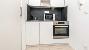 A compact kitchen with a microwave, oven, and a phone on the wall. - Charming Bright Gem Rovinj Downtown (Rovinj)
